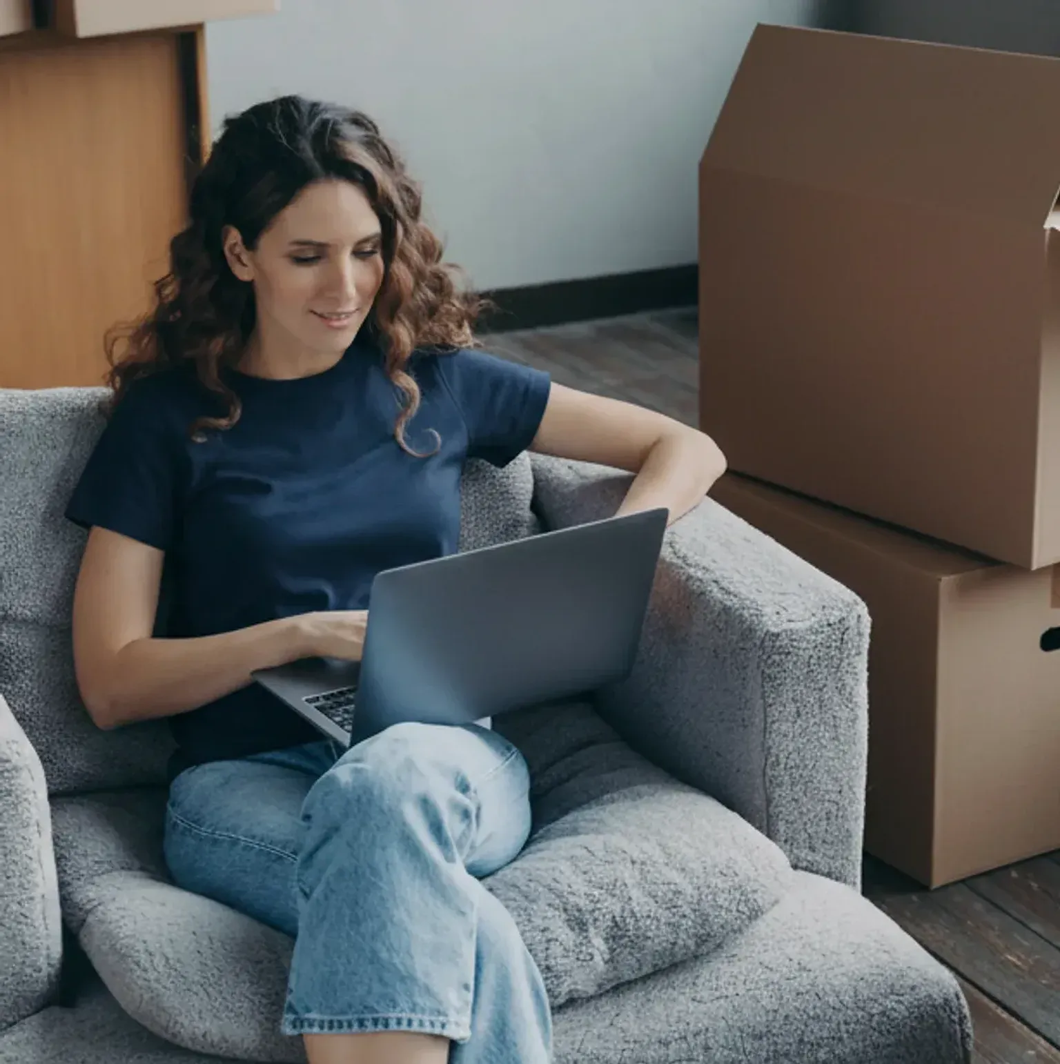 A person working on a laptop at home, surrounded by moving boxes